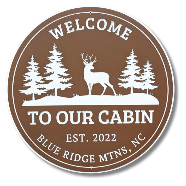 Brown round sign with white illustrations of three pine trees and a deer. Text reads: Welcome to Our Cabin, Est. 2022, Blue Ridge Mtns, NC. Ideal for those who appreciate cabin charm or rustic beach house decor. Product: Personalized Oval Custom Beach House Signs Coastal Decor.