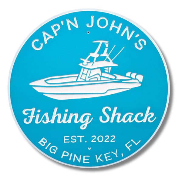 A personalized round beach house sign features white text and a boat graphic on blue. It reads: Capn Johns Fishing Shack, Est. 2022, Big Pine Key, FL. This item is listed as the Personalized Custom Round Beach House Sign Coastal Decor.