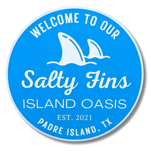 Blue circular Personalized Custom Round Beach House Sign Coastal Decor with white text: Welcome to our Salty Fins Island Oasis, Est. 2021, Padre Island, TX. Features two stylized shark fins.