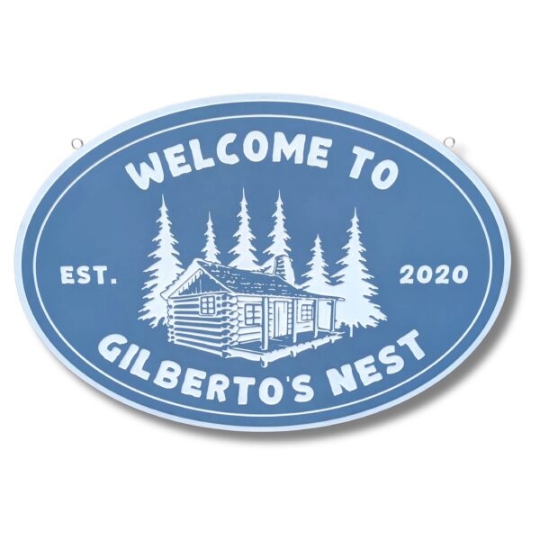 The Personalized Oval Custom Beach House Sign in blue with white text says Welcome to Gilbertos Nest, Est. 2020, and portrays a quaint cabin amidst trees, reminiscent of classic coastal decor.