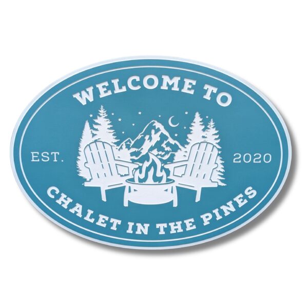 Oval sign with Welcome to Chalet in the Pines in white on a blue background. Styled like charming beach house signs, it features two Adirondack chairs, a fire pit, pine trees, and mountains. Part of the Personalized Oval Custom Beach House Signs Coastal Decor collection. Established 2020.