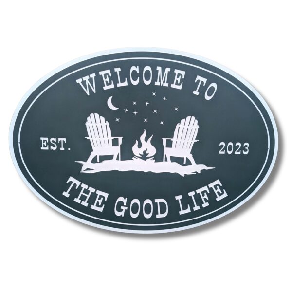 The Personalized Oval Custom Beach House Signs Coastal Decor features Welcome to the Good Life, with Adirondack chairs by a campfire under a crescent moon and stars. It evokes serenity and includes EST. 2023 on either side for a charming touch.