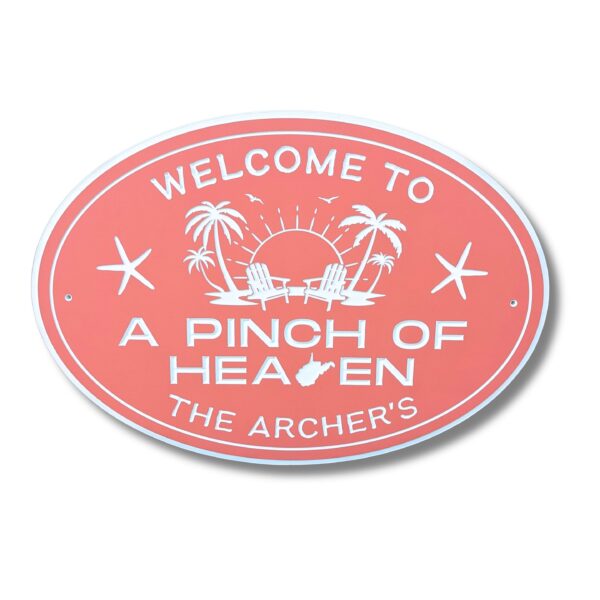 A pink oval sign with white text says, Welcome to a Pinch of Heaven, The Archers. This charming Personalized Oval Custom Beach House Sign includes palm trees, two chairs, a sun with rays, and birds in flight.