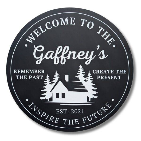 The Custom Carved Round PVC Cabin Sign displays Welcome to the Gaffneys with a house and trees graphic. It includes the phrase, Remember the past, create the present, inspire the future. Est. 2021.