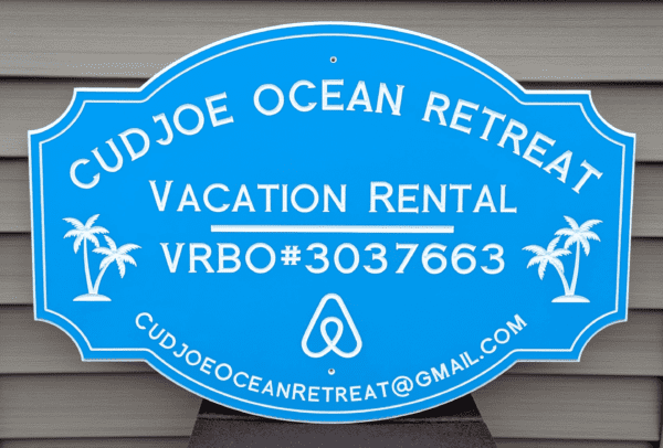 Custom PVC sign for Cudjoe Ocean Retreat, featuring a blue background with white engraved text and graphics. Includes vacation rental details, VRBO#3037663, email address, and palm tree illustrations, emphasizing weatherproof durability and elegance.